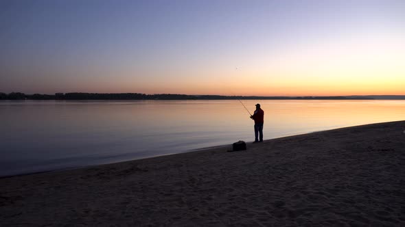 A Man Is Fishing at Sunrise By the River. The Yellow Sun Rises From the Horizon. Silhouette of a alt