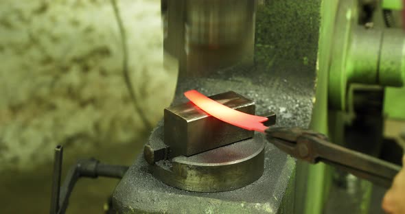 Bladesmith working with hot blade at hydraulic press alt