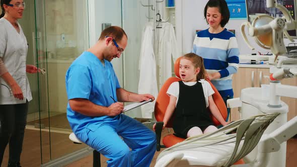 Nurse Taking Notes on Clipboard About Little Girl Dental Problems alt
