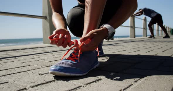 Fit woman tying shoelaces on a promenade at beach 4k