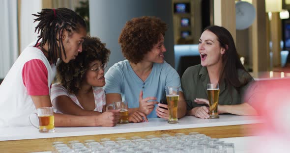 Diverse group of happy friends drinking beers and using smartphone at a bar alt