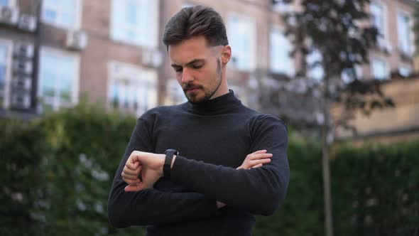Portrait of Serious Caucasian Young Businessman Checking Time on Wristwatch Looking Around Standing alt