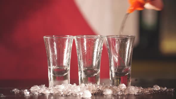 Barman Hand Pours Vodka in Short Transparent Glasses with Ice Chips for Cooling alt