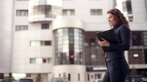 Young Attractive Business Woman Running Through the City with Documents Talking on the Phone alt