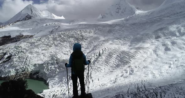 Woman backpacker hiking in high altitude winter mountain top facing the glacier mountains alt