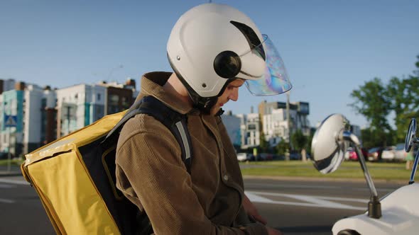 A Delivery Man in a Helmet on a Scooter Who Checks the Delivery Address on the Phone alt