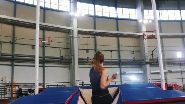 Pole Vaulting Indoors - a Young Woman with Ponytail Running Up and Jumping Over the Bar - Touches alt