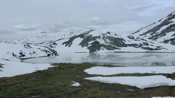 Aerial Top notch Drone Fly above the clearing of frozen lake Isoba, rocky and snowy trekking route, alt