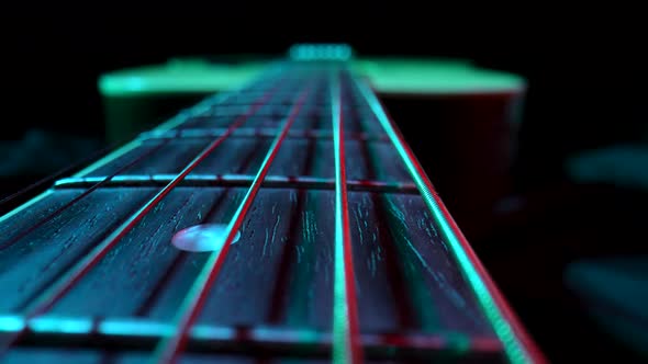 Fretboard of Classical Acoustic Guitar Against Black Background Illuminated By Blue and Red Light alt