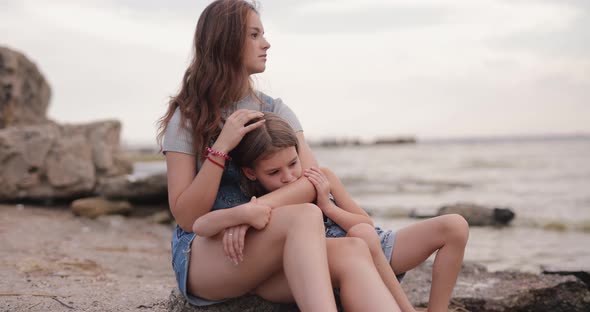 Two Cute Sisters Sitting at the Beach of the Sea and Relaxing alt