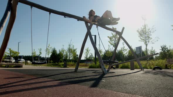 Young Beautiful Brunette Woman with Flowing Hair in Tightfitting Black Tracksuit Rides on Children's alt