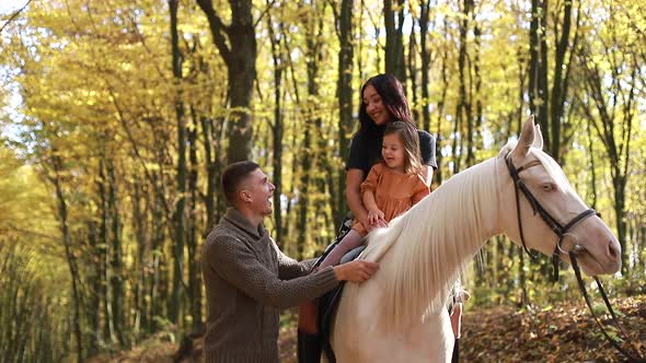 Young family walking with white horse in autumn forest, slow motion alt
