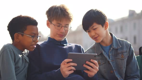 Diverse Schoolboys Using Digital Tablet on Bench at School Outdoors alt