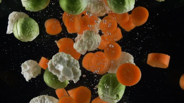 Mix of Vegetables Falls Into the Water on a Black Background