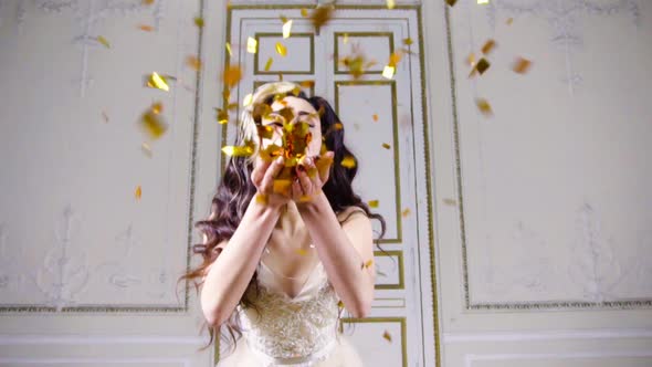 Young Brunette Woman with Red Lips Blows Gold Confetti alt