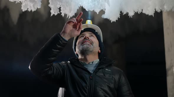 Portrait of Excited Caucasian Man in Helmet with Flashlight Admiring Beauty of Ice Outdoors at Night alt