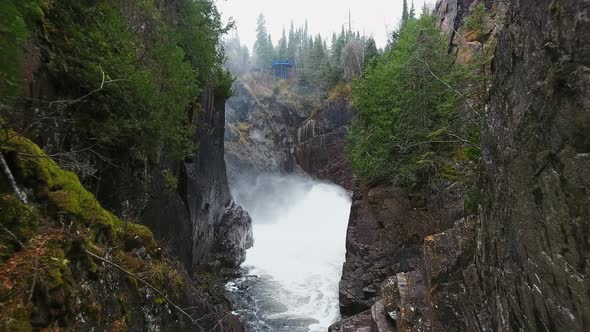 Drone camera approaches stormy waterfall in wooded hills in Aguasabon Falls, Ontario, Canada alt