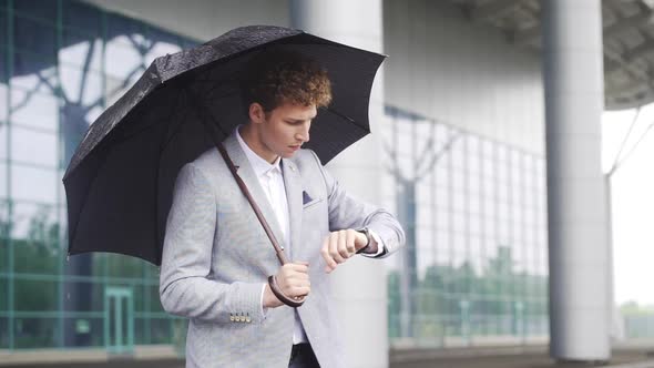Corporate Man Businessman Waiting for Taxi Under Rain Holding Umbrella Checking Time on Wrist Watch