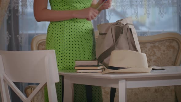 A Girl in a Dress Puts a Bag on the Table and Lays Down Her Hat a Notebook and a Pen From the Bag alt