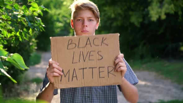 a Young Caucasian Teenager in a Blue Shirt Holds a Cardboard Box with Handwritten Text BLACK LIVES alt