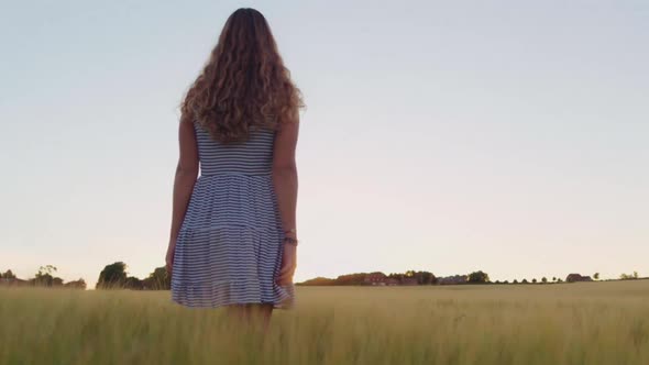 Woman In Striped Dress Walking Through Field At Sunset alt