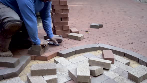 Brick paving expert fits brick paver into place and measures it and marks it for cutting while weari alt