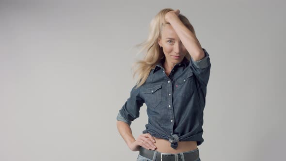 Young Beauty Blonde Woman in Studio Wears Classic Denim with Blowing Hair
