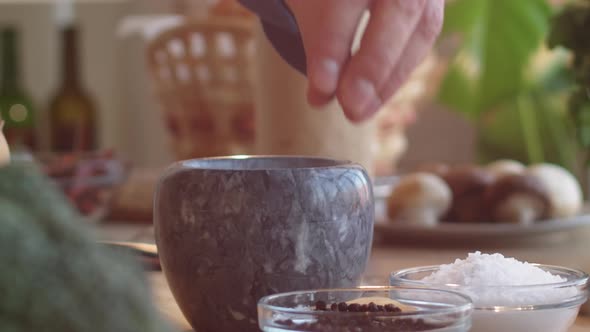 Hand of Male Chef Pouring Black Peppercorns into Mortar alt