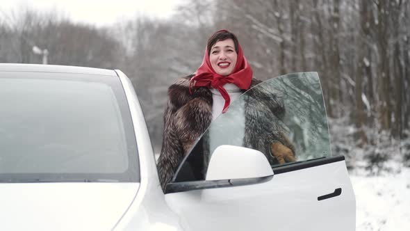 Stylish Woman in Fur Coat Sitting Into the White Gybrid Car alt