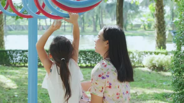 Mother helps her little daughter to hang on colorful monkey bars in the playground. alt