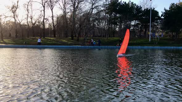 Beautiful handmade sailboat swims in a pond in a park. alt