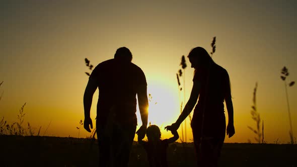 Parents with Kid Holding Hands Walking at Sunset alt