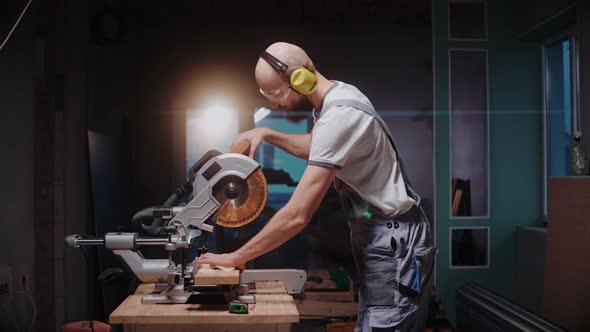 A Builder Cuts a Wooden Board on a Table Circular Saw in Construction Studio