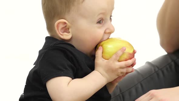 Baby Eats an Apple, Next To Her Mother. White Background. Slow Motion. Close Up alt