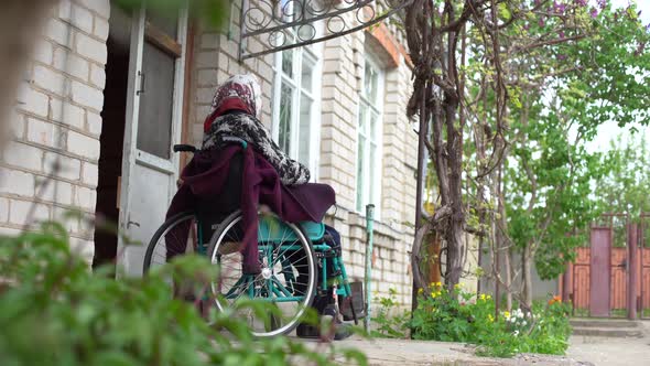 Old Lonely Woman Sitting in a Wheelchair Near the Window in His House