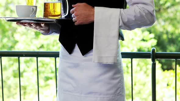 Male waiter holding tray with coffee cup and beer mug in restaurant alt