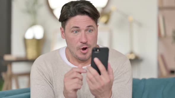 Middle Aged Man Celebrating on Smartphone at Home alt