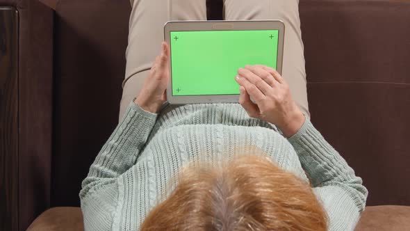 Aged woman with a tablet PC (green screen) on a sofa