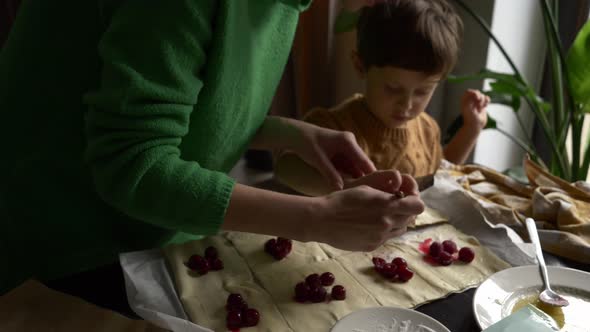 Mother with a son cooking cookies with a cherry at home.