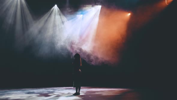 an enchanted girl stands in smoke and beautiful lighting on the stage in the theater and looks with