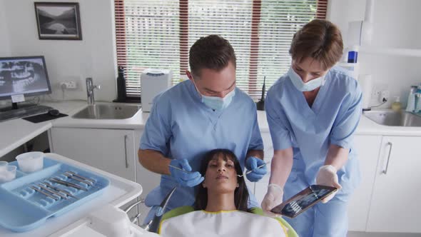 Caucasian male dentist with face mask examining teeth of female patient at modern dental clinic alt