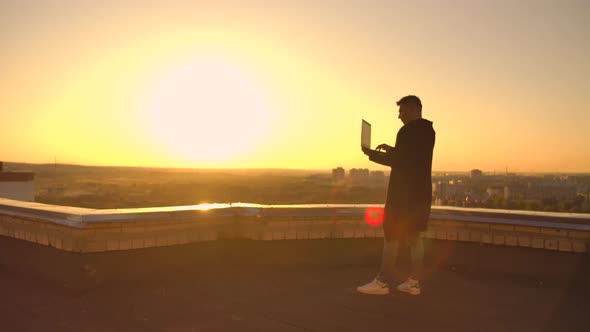 Hacker Using Laptop on Rooftop with City View and Forex Chart. Hacking and Stats Concept alt