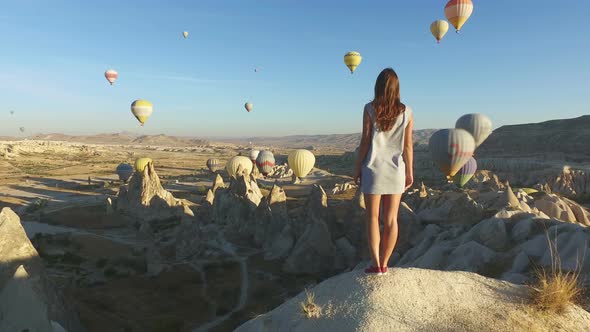 Woman on Edge of Rock and Looking at Hot Air Balloons, Cappadocia, Turkey.