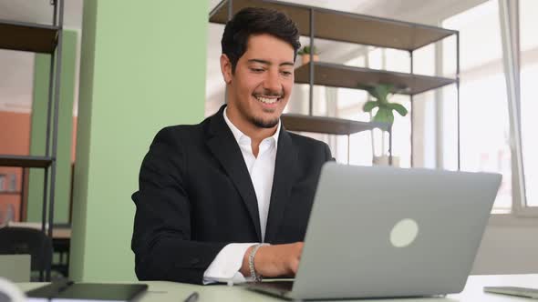 Optimistic Ethnic Man in Formal Business Wear Using Laptop Sitting on the Workplace