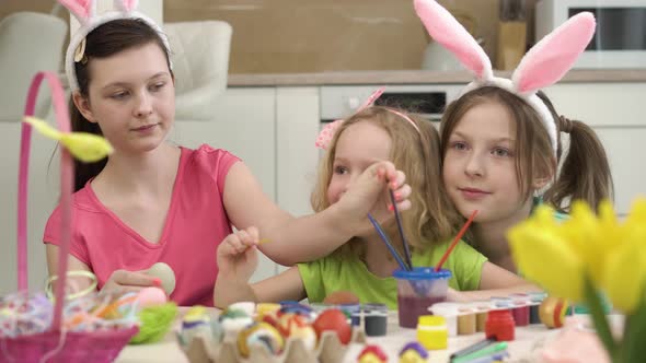 The Girl Helps and Teaches Her Sister to Paint Easter Eggs with Paint