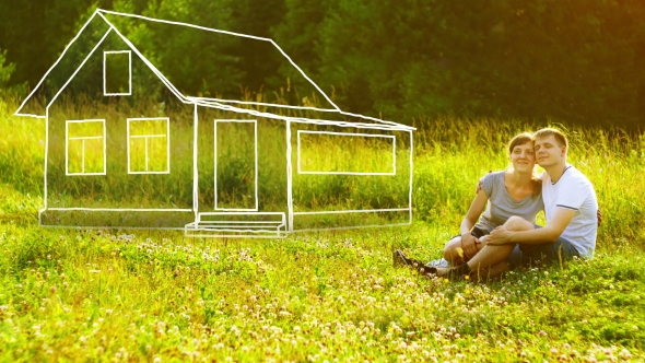 Young Happy Couple Sitting on Green Grass in Park and Dreaming About They Own House. Mortgage
