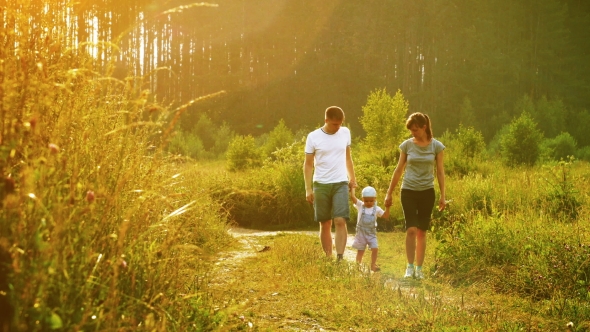 Young Family Walking on Rural Footpath and Holding Hands Them Baby on Sunset Time.