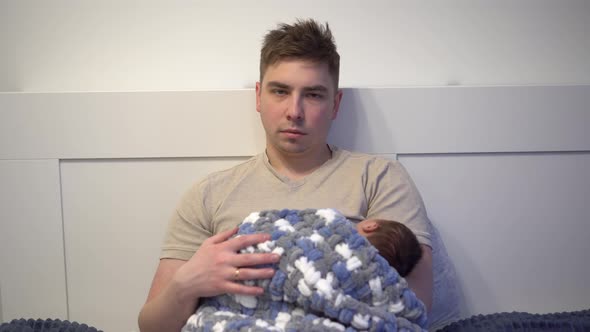 An Exhausted Young Dad Cradles a Child in His Arms in Bed alt