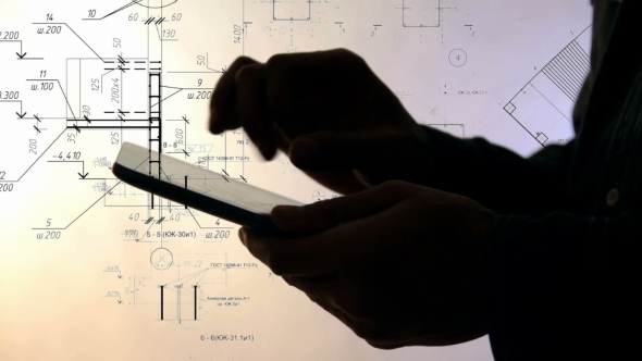 Silhouette of Hands Using Tablet PC While Working with Blueprints. alt