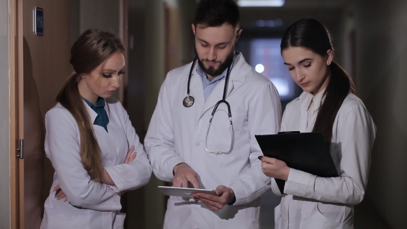 Doctor in Hospital Corridor Interns Explains That a Patient Receives. Doctor with Two Girls Interns